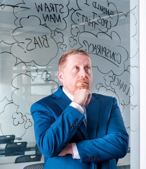 A professor stands pondering in front of glass whiteboard